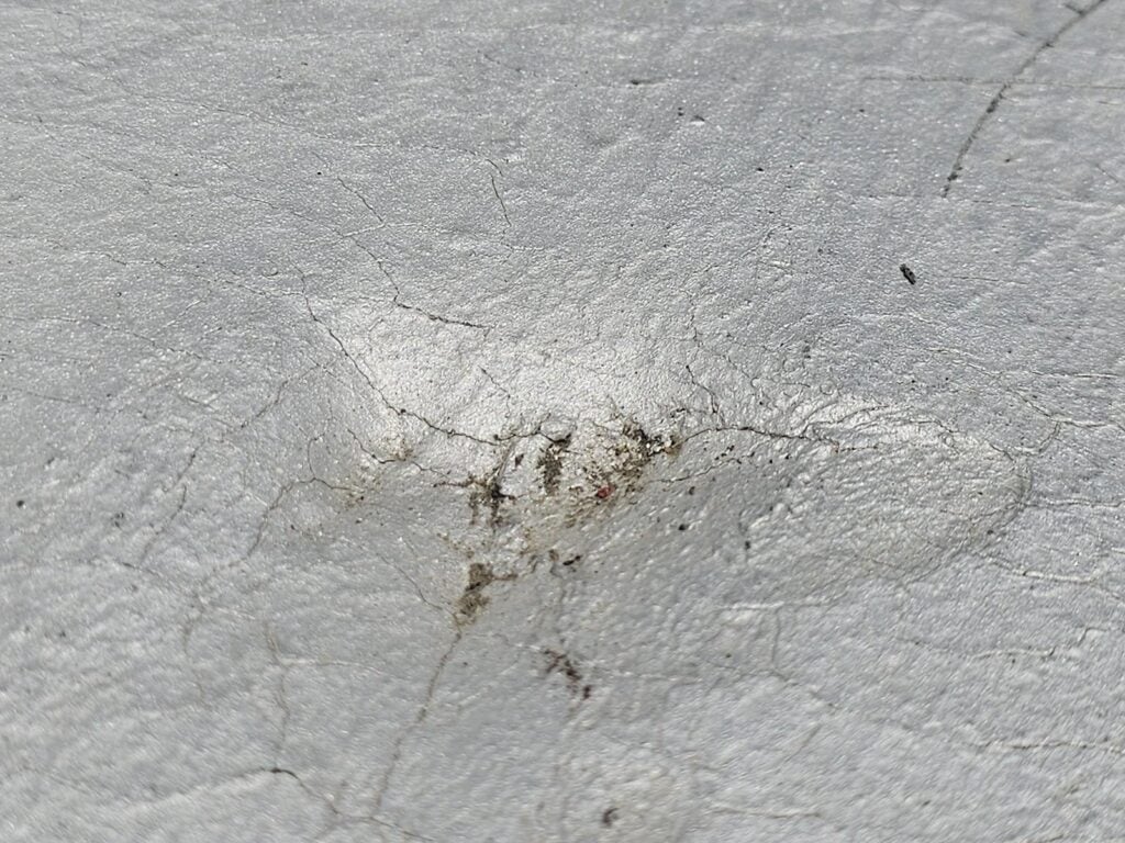 Close-up of HVAC impact divot with radiating cracks on modbit membrane, Washington DC