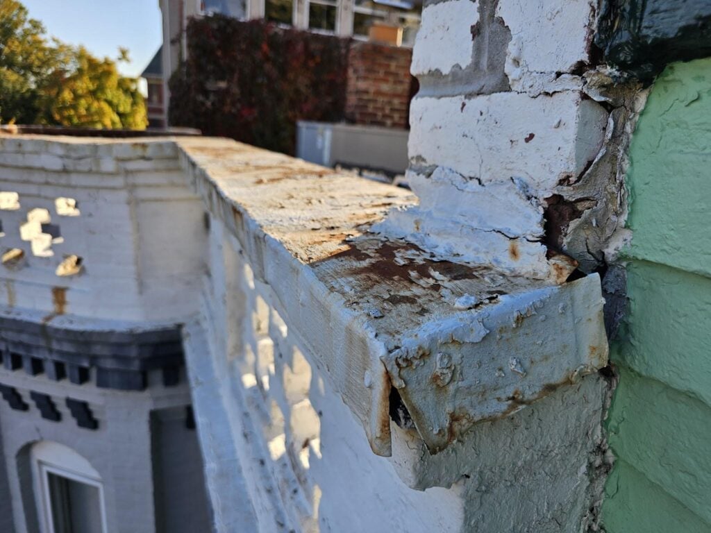 Red rust and oxidation visible on ferrous metal coping protecting a masonry parapet wall in Washington DC