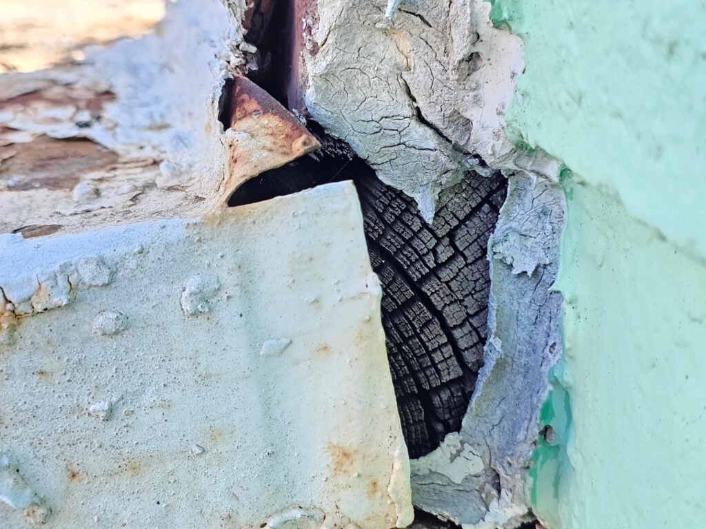 Exposed wooden nailer board end grain showing moisture damage and deterioration beneath a ferrous metal roof flashing in Washington DC